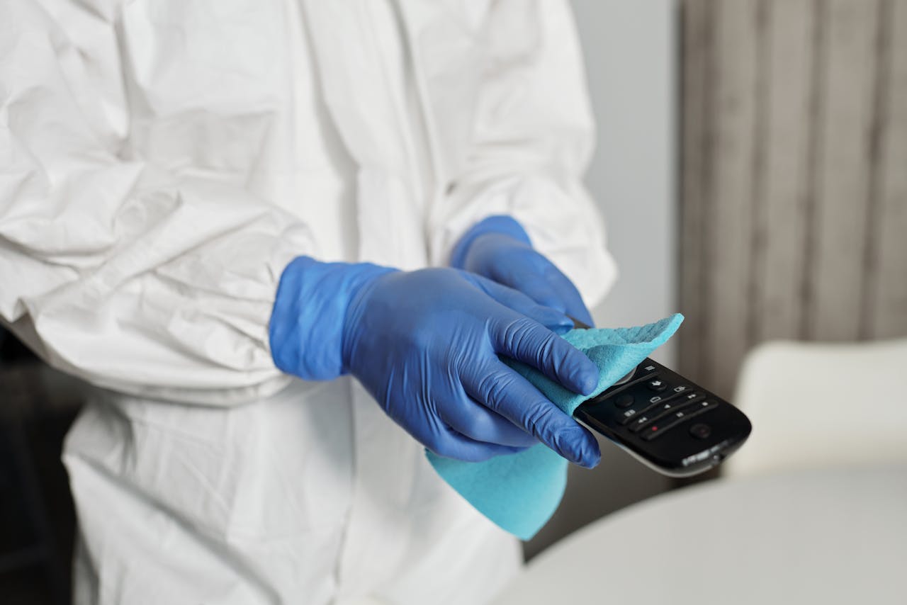 hero-img Close-up of a person disinfecting a remote control wearing protective gloves, ensuring cleanliness.